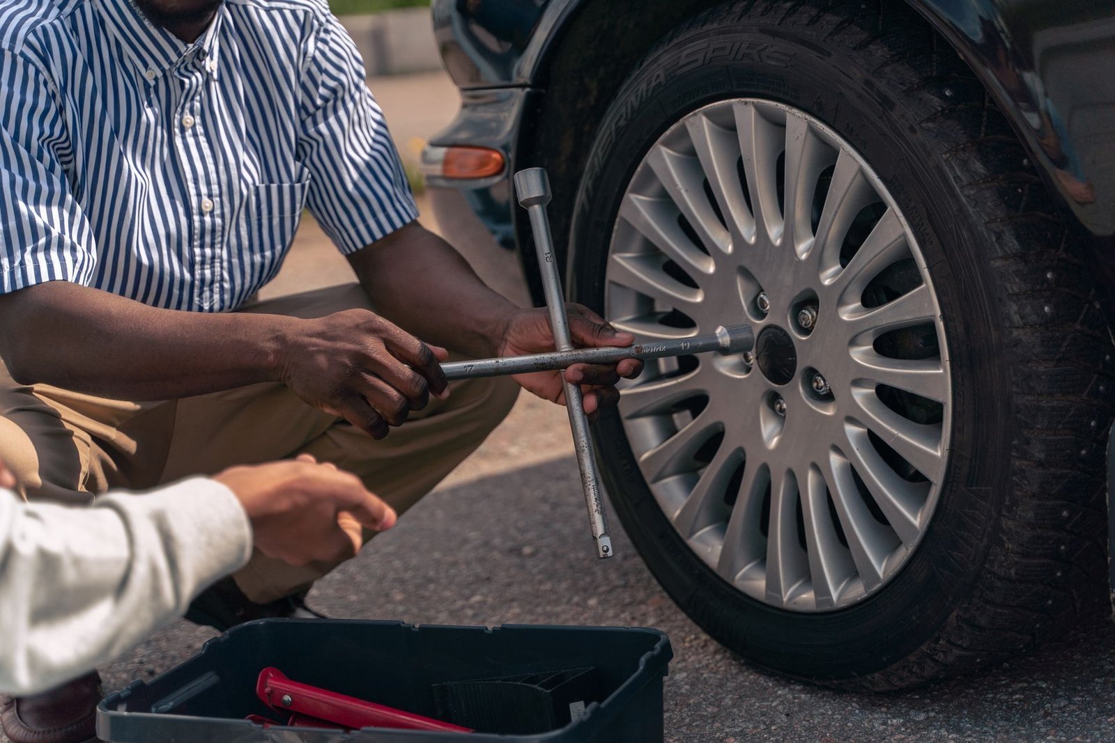 An adult shows a teenager how to change a wheel